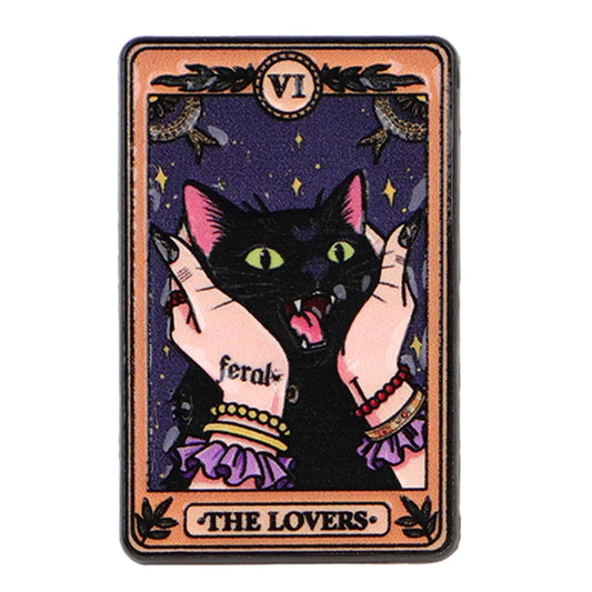 A tarot card style art print featuring a black cat with green eyes and pink ears, held by two hands with tattoos and bracelets against a dark purple starry background. The card has an ornate peach border with the Roman numeral VI at the top and the text 'THE LOVERS' at the bottom.